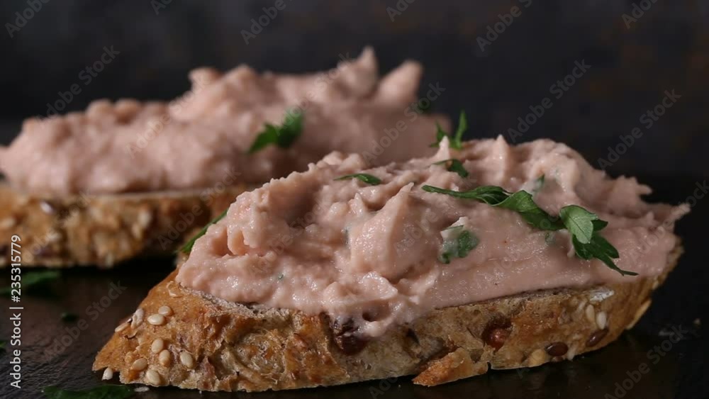 Spreading chopped parsley over two slices of bread with vegetable pate made from mushrooms and other vegetables 