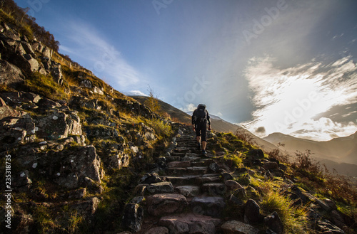 Hiker climbing steep steps at Ben Nevis, Scotland's highest mountain, during early morning with first sunlight photo