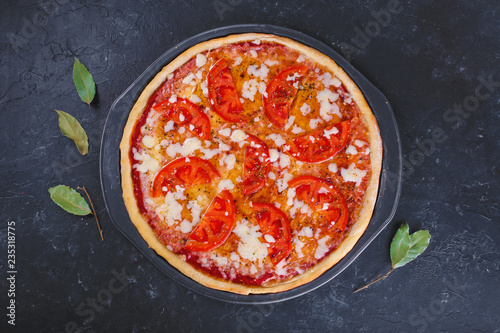 pizza Margherita with cheese and tomatoes on a dark background
