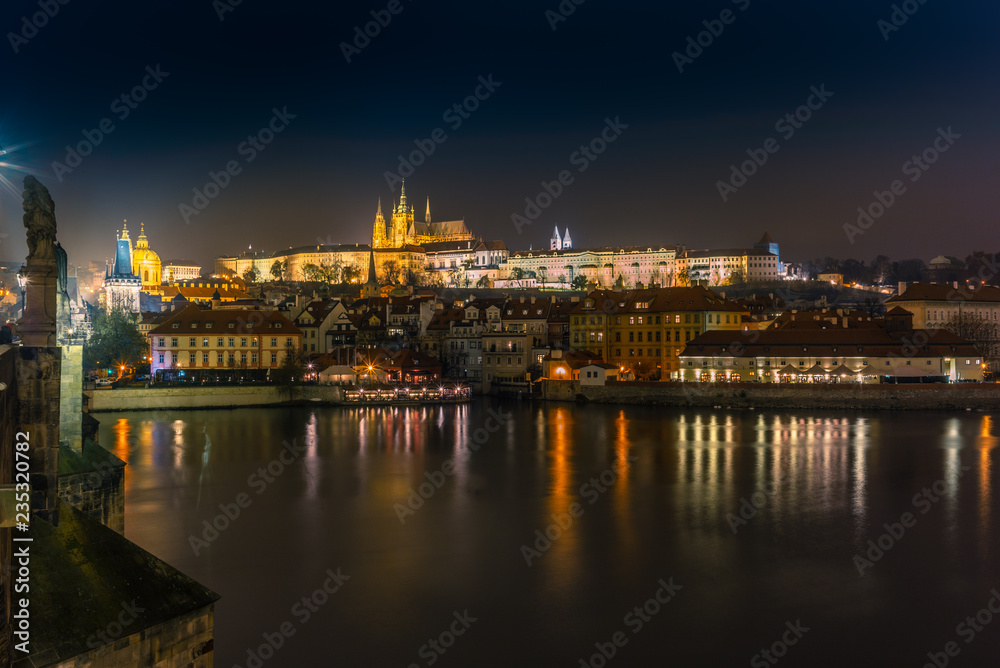 View f the skyline of Prague's castle and the riverside buildings and street lights reflecting on the Vltava river in a cold winter night