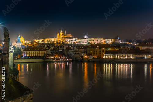 View f the skyline of Prague s castle and the riverside buildings and street lights reflecting on the Vltava river in a cold winter night