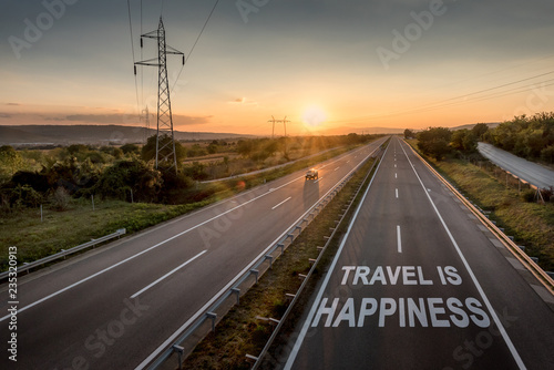 Beautiful Countryside Motorway with a Single Car at sunset with motivational message Travel Is Happiness