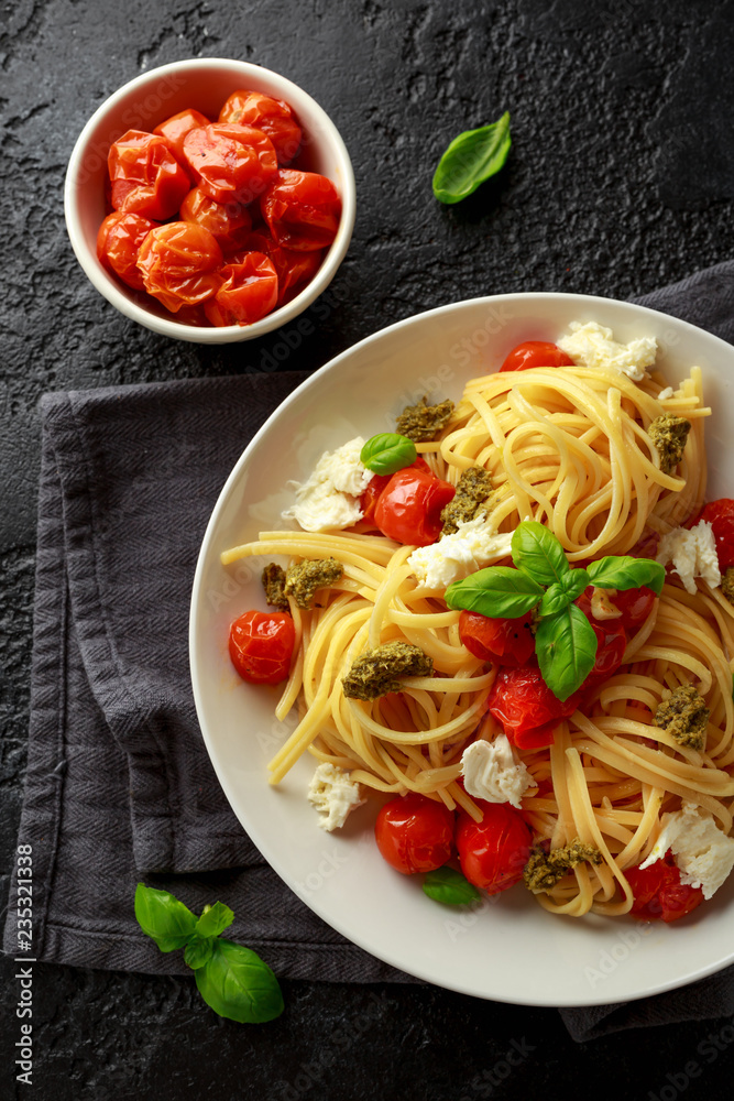 Pasta with green pesto sauce, roasted cherry tomatoes and mozzarella cheese in white plate on dark rustic background Pasta with green pesto sauce, roasted cherry tomatoes and mozzarella cheese in white plate on dark rustic background