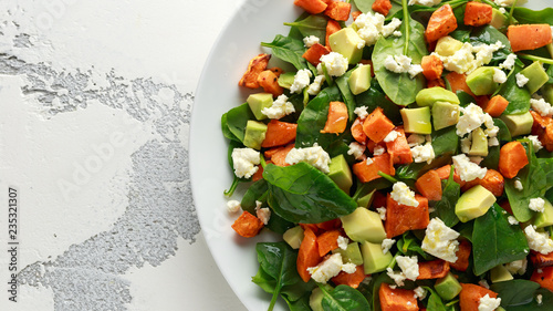 Avocado, roasted sweet potato, spinach, feta cheese healthy salad in white plate.