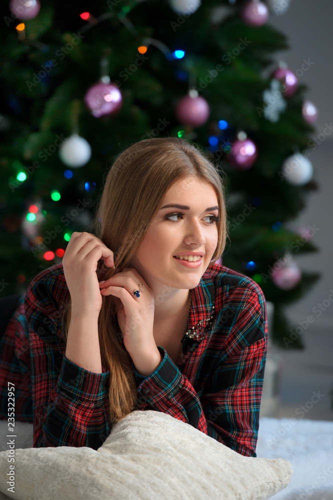 Portrait of happy beautiful girl on bed at home with decorated Christmas tree in background Portrait of happy beautiful girl on bed at home with decorated Christmas tree in background