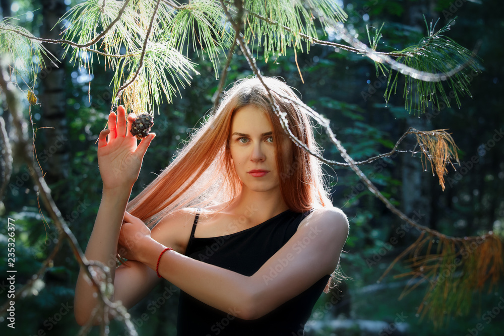 Beautiful girl with long hair poses with a cedar cone in the Siberian taiga
