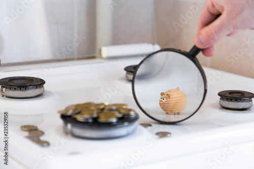 the concept of spending on utilities. toy pig through a magnifying glass looks at the scattering of coins that are on the burner