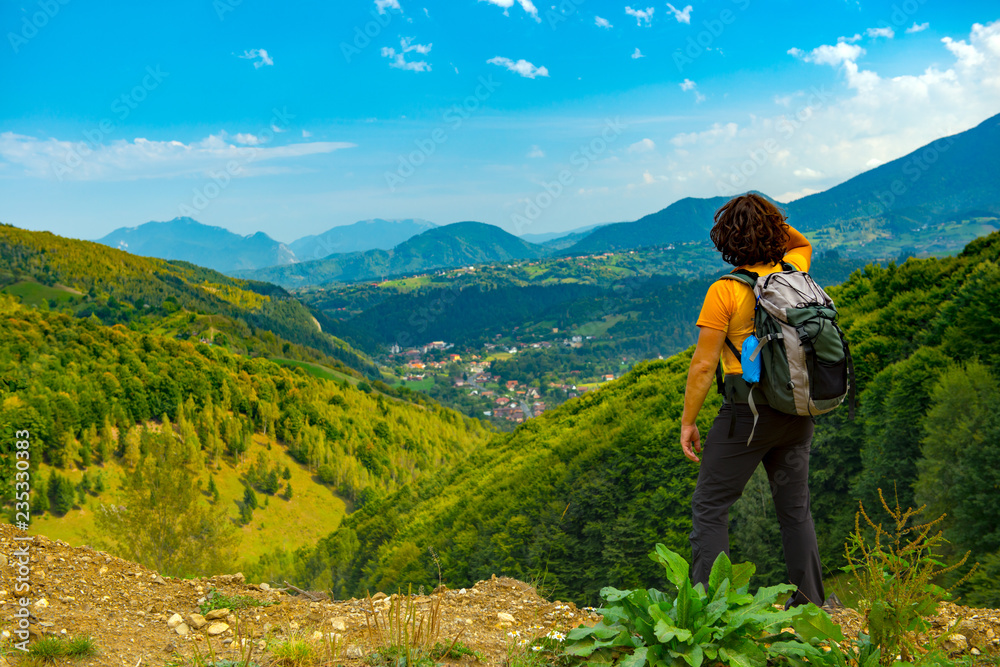 Young mountain hiker enjoying a beautiful mountain landscape covered with lush forests. Hiking in a sunny summer day.