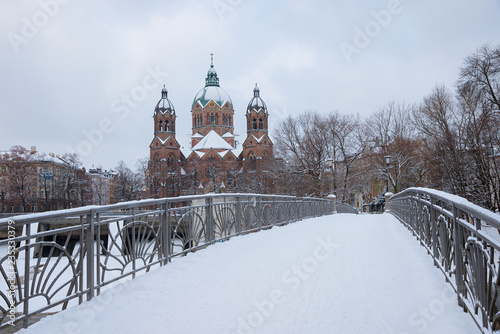 verschneite Brücke über die Isar, Kabelsteg genannt, mit Blick zur Lukaskirche im Winter
