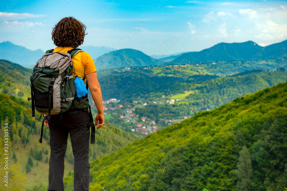 Young mountain hiker enjoying a beautiful mountain landscape covered with lush forests. Hiking in a sunny summer day.