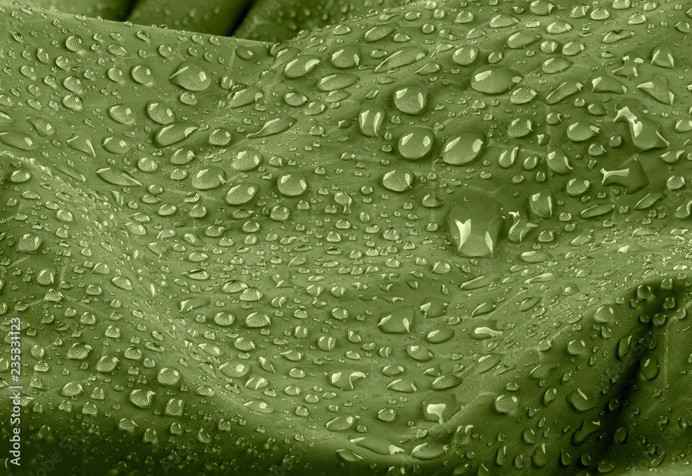 Water drops on waterproof green nylon fabric. Macro detail view of texture of woven synthetic waterproof clothing. Waterproof fabric with waterdrops.