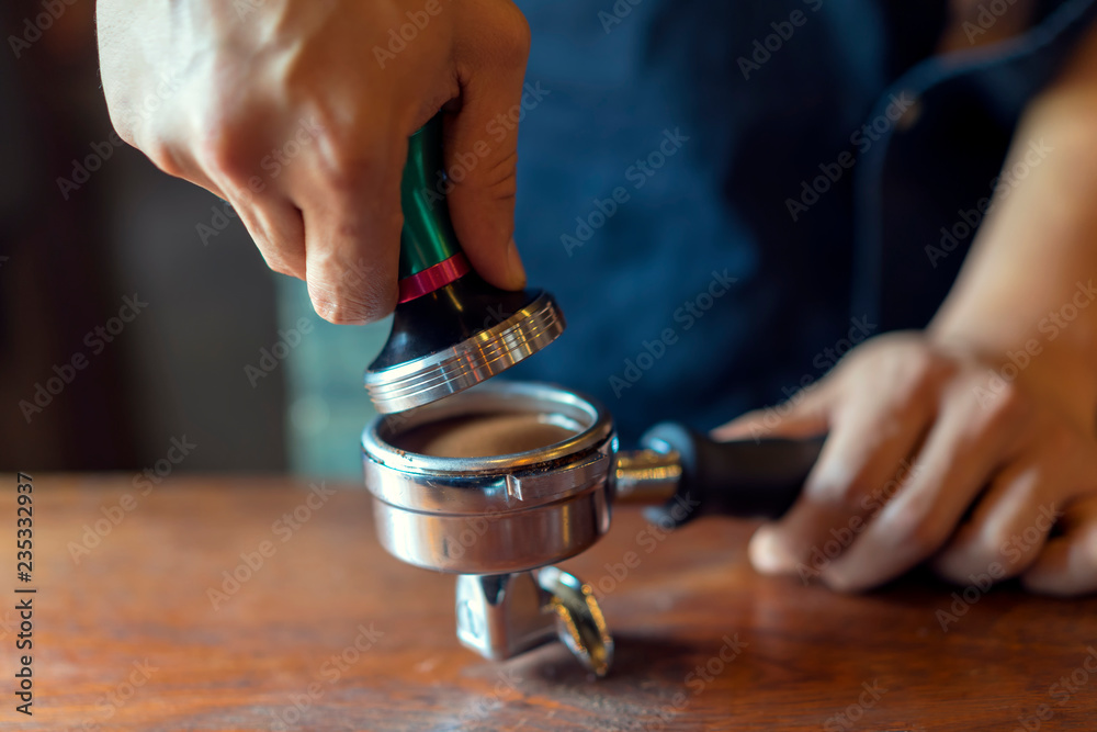 Barista presses ground coffee using tamper, prepares espresso in his coffee shop. Barista presses ground coffee using tamper, prepares espresso in his coffee shop.