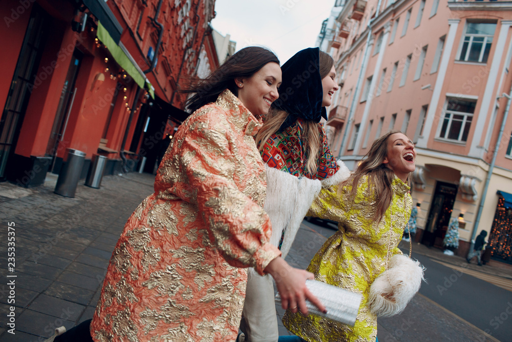 Three young stylish women are laughing and walking down the street.