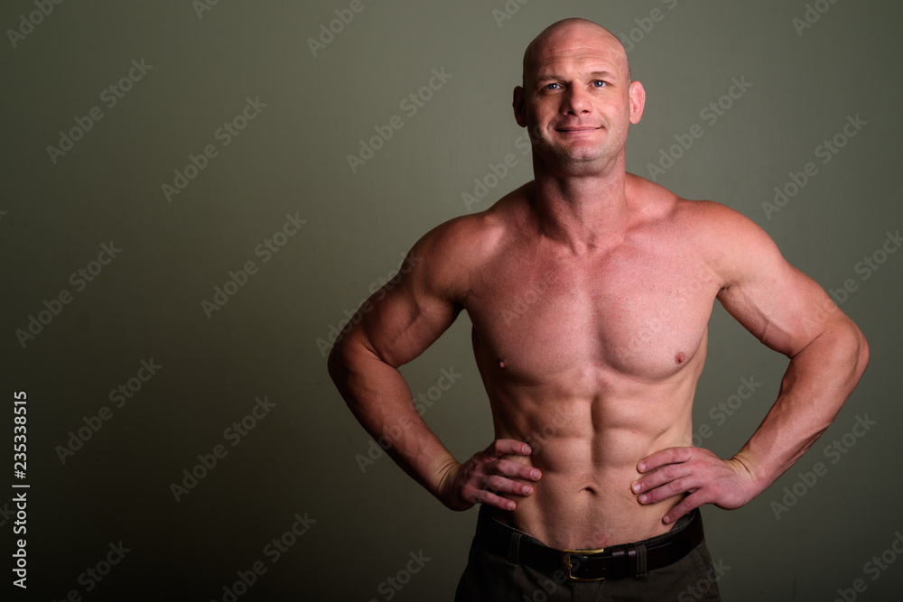 Bald muscular man shirtless against colored background