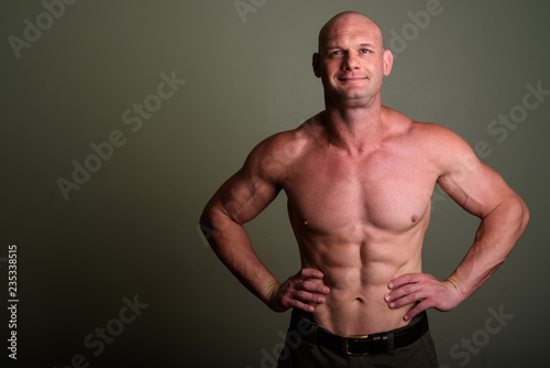 Bald muscular man shirtless against colored background