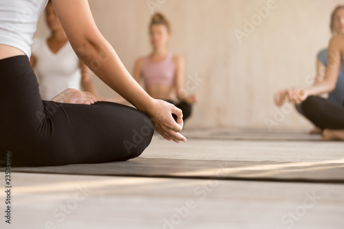 Young yogi sporty woman practicing yoga, instructor and group doing Sukhasana exercise, meditating in Easy Seat pose, working out indoor at yoga studio, close up. Well being, wellness concept