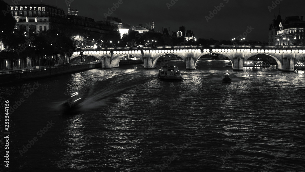 Night view of Seine river with Pont Neuf bridge, touristic ship and two police boats coming to the rescue. Paris, France. Black and white photo.