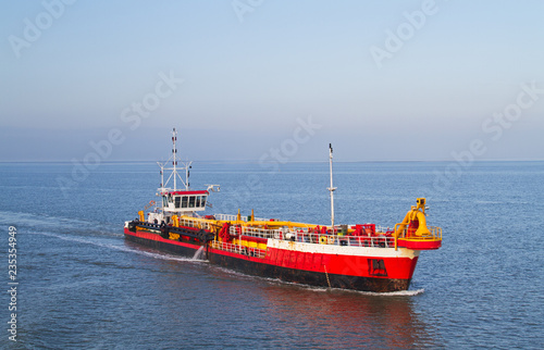 Red dredging vessel working on sea, removing sediment in a waterway