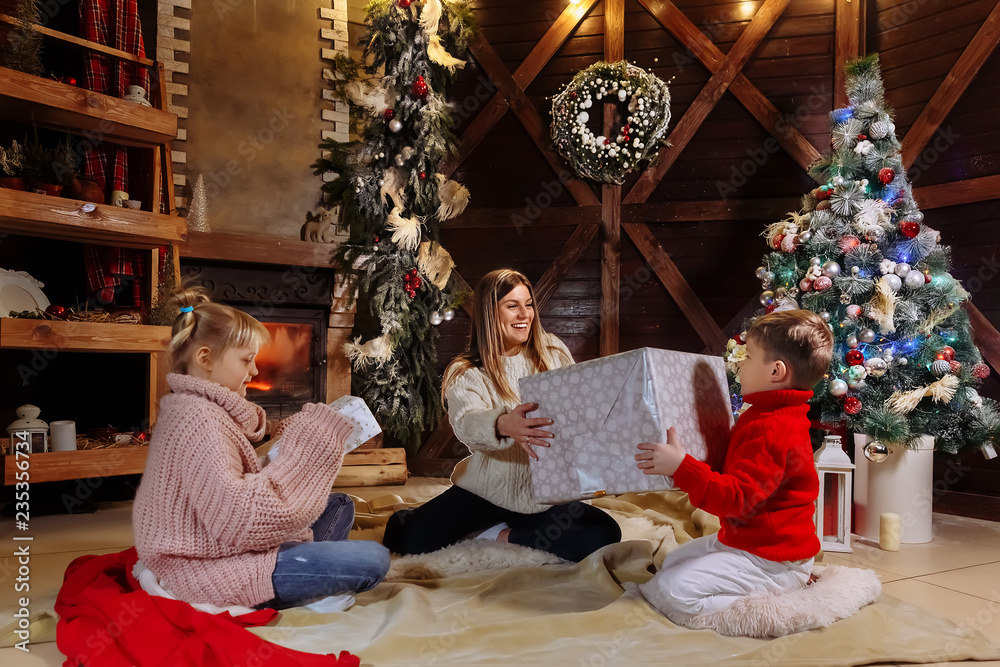 Merry Christmas and Happy New Year. Cheerful mom and her cute daughter and son exchanging gifts. Parent and children having fun near Christmas tree indoors. Loving family with presents in room. Merry Christmas and Happy New Year. Cheerful mom and her cute daughter and son exchanging gifts. Parent and children having fun near Christmas tree indoors. Loving family with presents in room.