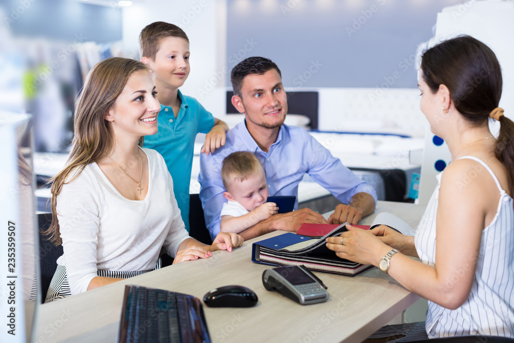 Fototapeta premium Young smiling family choosing material for mattress with saleswoman