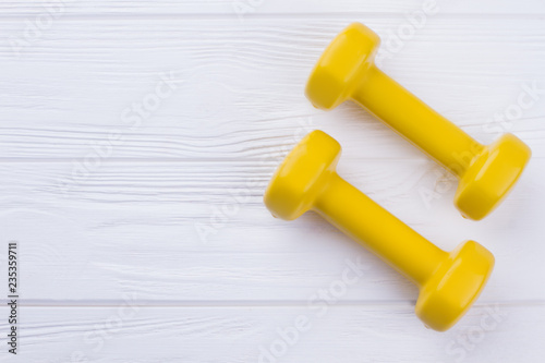 Two yellow dumbbells on wooden background. Pair of dumbbells with copy space. Diet and fitness concept.