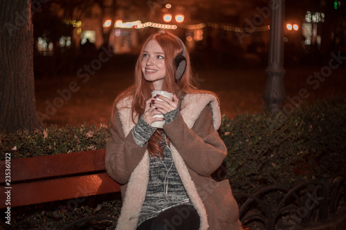 The portrait of an young smiling redhear lady on the evening wearing earmuffs photo