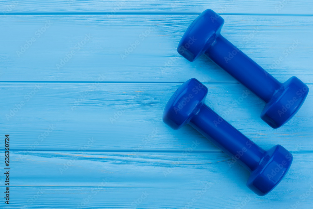 Blue dumbbells and copy space. Pair of small dumbbells on color wooden surface with text space. Beginner gym workout equipment. Blue dumbbells and copy space. Pair of small dumbbells on color wooden surface with text space. Beginner gym workout equipment.