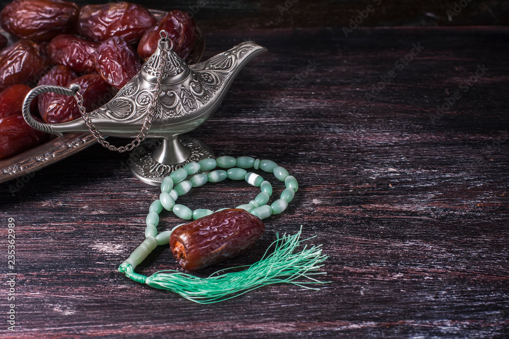 Fototapeta premium Green islamic prayer beads, dates and silver aladdin's lamp on a dark wooden background. Ramadan concept.