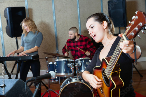 Attractive female soloist playing guitar and singing with her music band in sound studio photo