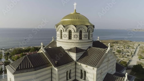 View of the big white church with golden domes in front of beautiful river, spring Vologda, Russia. Shot. Beautiful aerial from the bird's eye view for the big church on the river bank. photo