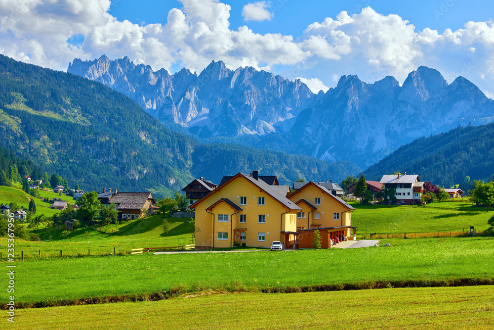 Austrian village among meadows fields and Alpine mountains.