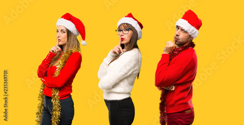 A group of people Blonde woman dressed up for christmas holidays showing a sign of closing mouth and silence gesture on yellow background