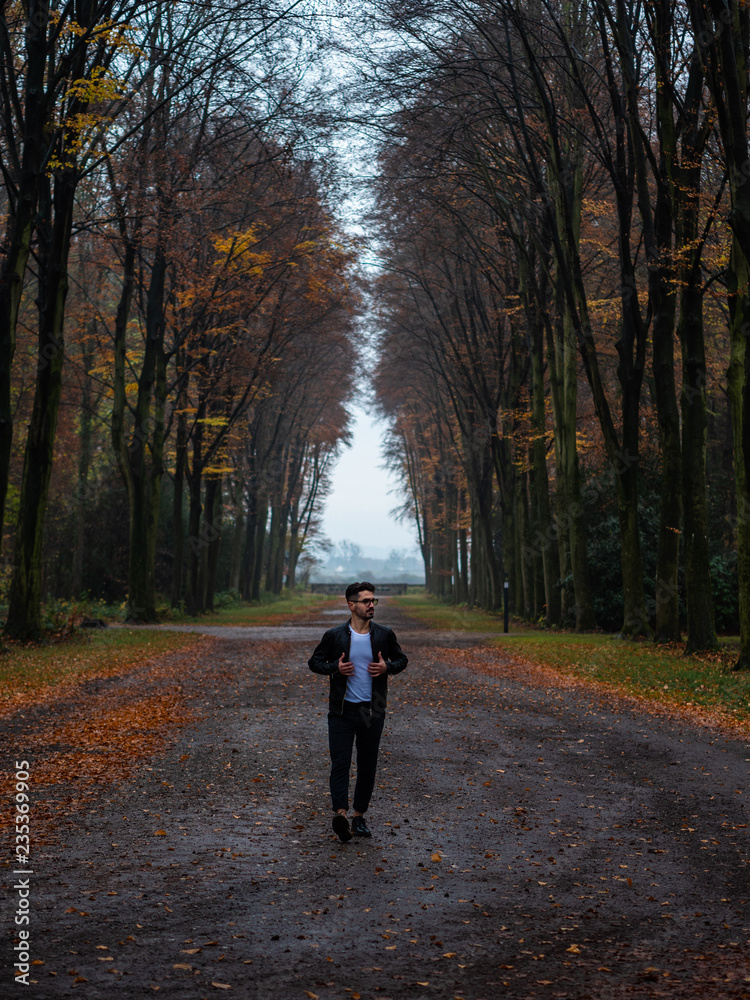 young man with glasses walking in a tunnel of trees young man with glasses walking in a tunnel of trees