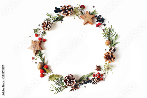 Christmas circle floral composition. Wreath of cypress, eucalyptus branches, pine cones, rowan berries, anise, confetti stars and sea holly flowers on white background. Winter wedding design. Flat lay