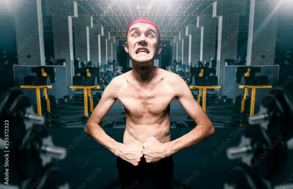 Thin guy poses on workout in gym, dystrophic - obrazy, fototapety, plakaty 