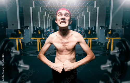 Thin guy poses on workout in gym, dystrophic photo