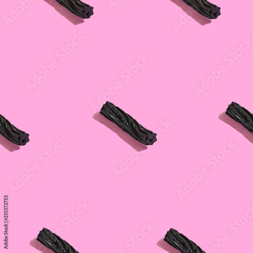 Creative seamless pattern with black liquorice candy on pink background. Sweet abstract background