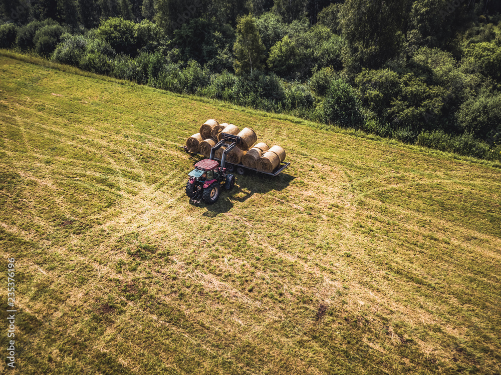 Obraz premium Aerial Drone Photo of Farmer Harvesting Hay Rolls in the Wheat Field with a Red Tractor