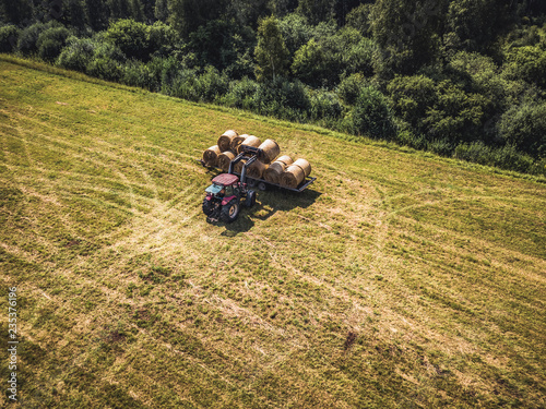 Aerial Drone Photo of Farmer Harvesting Hay Rolls in the Wheat Field with a Red Tractor