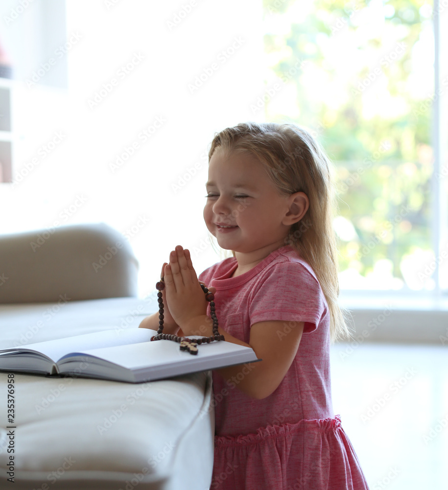 Cute little girl with beads praying over Bible in living room Cute little girl with beads praying over Bible in living room