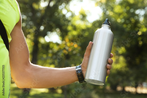 Young man holding bottle of water in park on sunny day, closeup