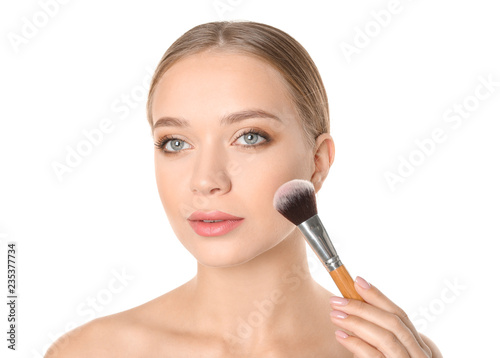 Portrait of beautiful young woman with makeup brush on white background