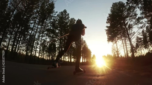 Training an athlete on the roller skaters. Biathlon ride on the roller skis with ski poles, in the helmet. Autumn workout. Roller sport. Adult man riding on skates. Shooting action cam. Slow motion. photo