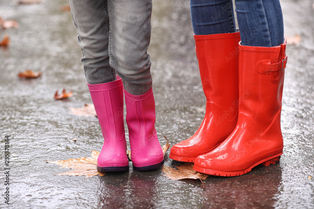 Mother and daughter wearing rubber boots after rain, focus of legs. Autumn walk
