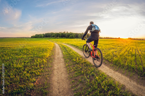 Cyclist on a dirt road in a field at sunset