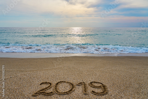 New year 2019 inscription written on the sand with waving sea on a sunset.