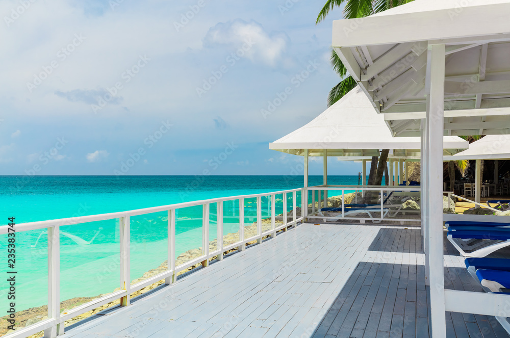 Obraz premium Varadero, Cuba, gorgeous amazing inviting view of a wooden deck with sun sheds near the beach, great view of tranquil turquoise tender ocean and cloudy bluish sky background