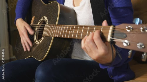 Caucasian woman strums acoustic guitar. Focus on strumming hand.