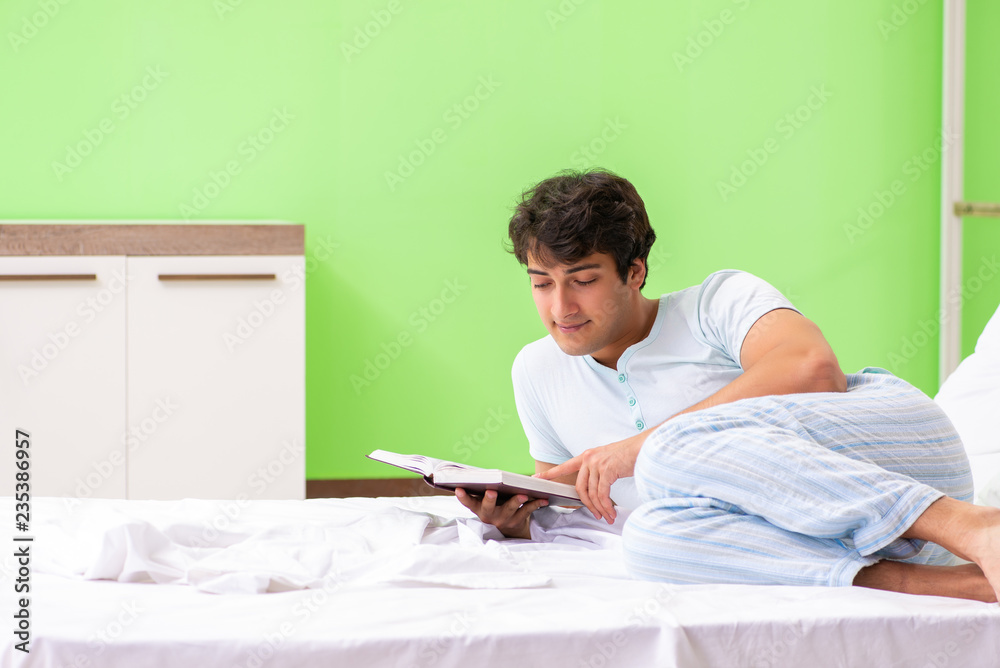 Young handsome student reading book in the bed 