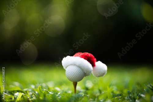 Festive-looking golf ball on tee with Santa Claus' hat on top for holiday season on golf course background
